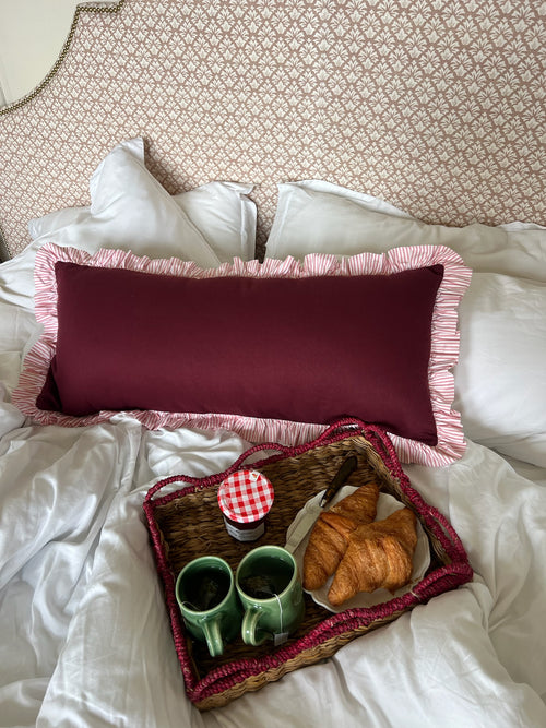 Breakfast tray with coffee and pastries on a bed with a big decorative ruffle pillow.