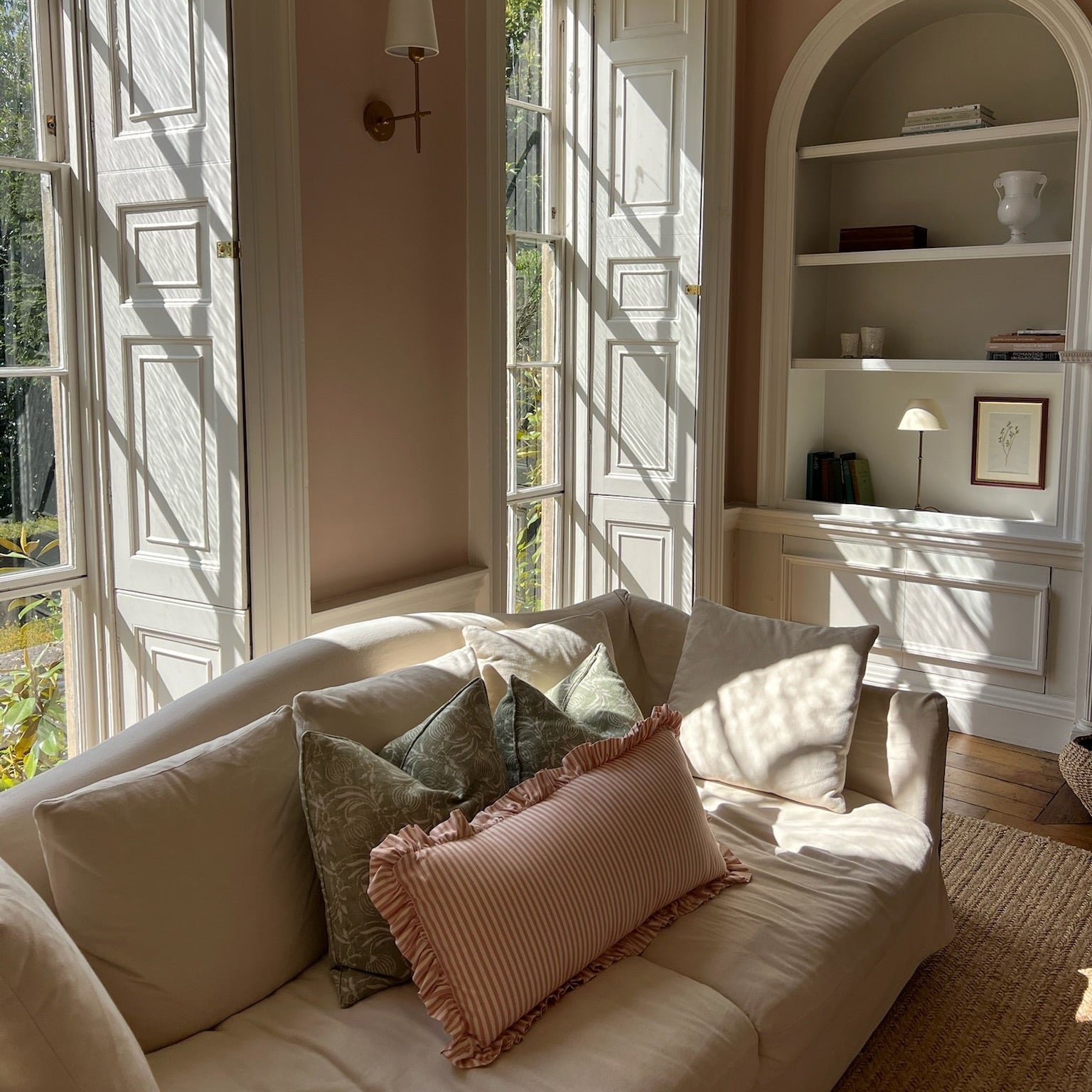 Living room with a beige sofa, decorative pink pillows, and a wall with built inshelves.